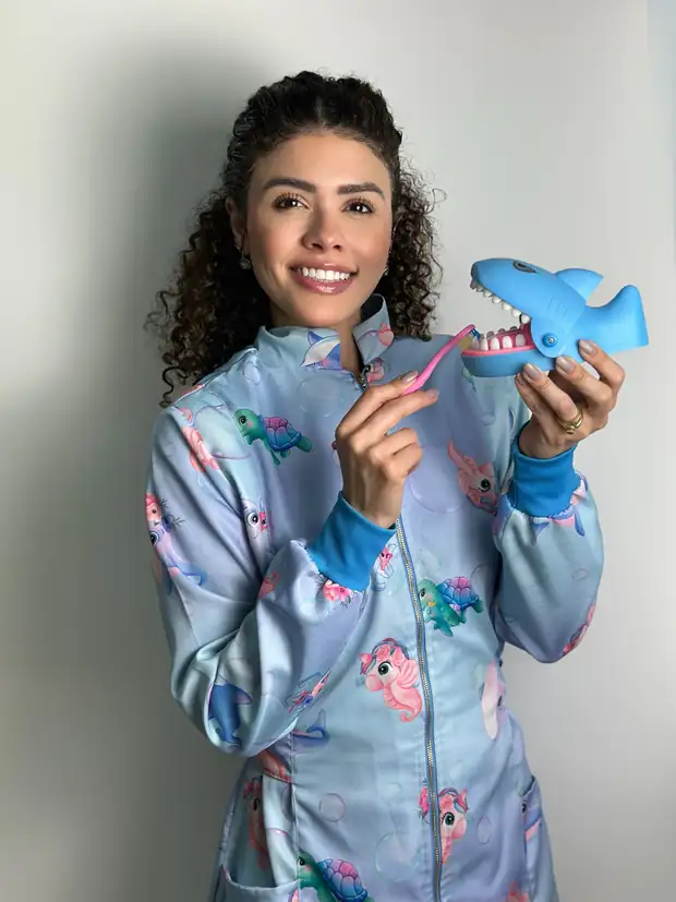 Dra. Gabriela Santos Barreto, odontopediatra no Tatuapé, sorrindo e ensinando a escovar os dentes num tubarão de brinquedo
